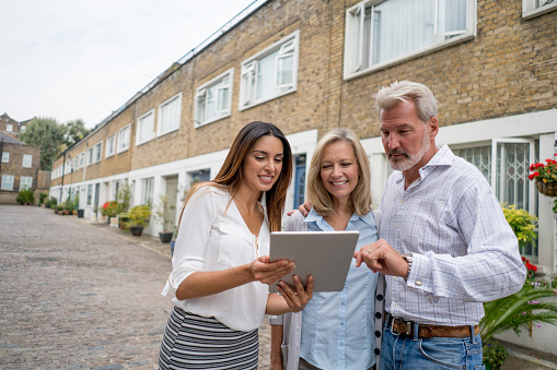 Real estate agent showing houses to a happy couple on her tablet computer