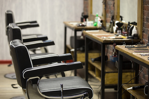Row of black leather chairs in modern barber shop interior. Horizontal indoors shot