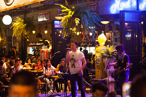 Bangkok, Thailand - October 1, 2016: Nightshot of a thai singer and band outside of a bar on night bazaar and train market Esplanade. People are sitting at tables around band and are listening music,