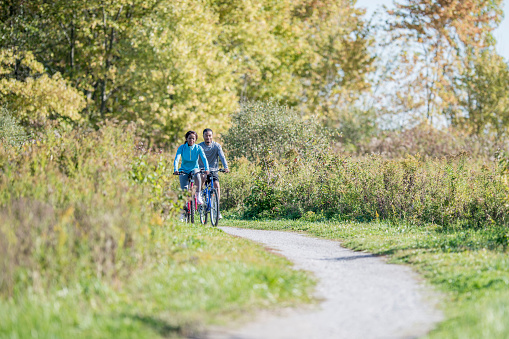 A young adult couple are biking together on path through the woods.