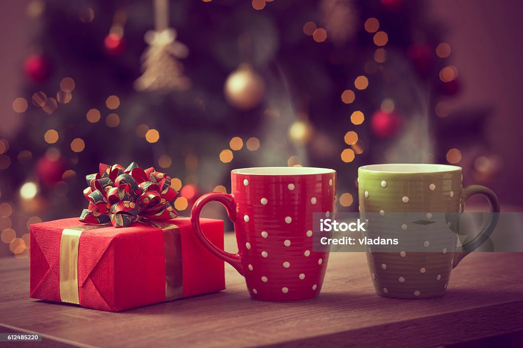 Christmas romance Nicely wrapped gift box and two cups of hot coffee set on the coffee table with the decorated Christmas tree in the background Christmas Stock Photo