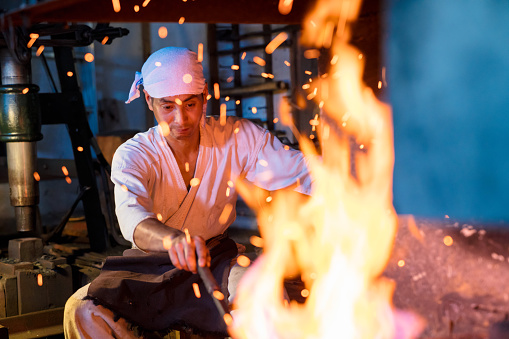 Japanese blacksmith stokes a fire preparing to forge a swordJapanese blacksmith stokes a fire preparing to forge a sword