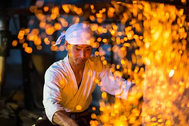 Japanese blacksmith stokes a fire preparing to forge a sword