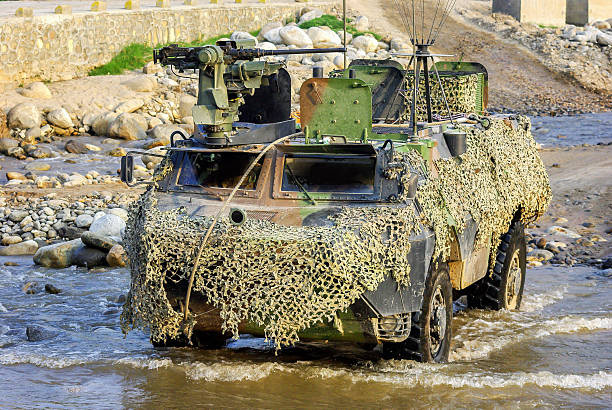 Horizontal color image of an military armored vehicle moving through river during sunny day.