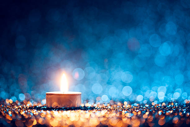 zapalona świeca na rozmytym niebieskim tle - christmas tea light - tea light zdjęcia i obrazy z banku zdjęć