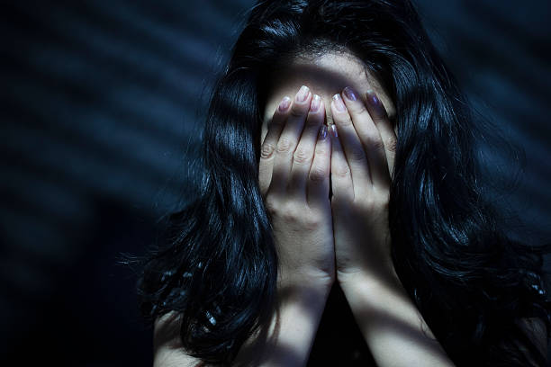 Woman covering face with hands and light coming through blinds. stock photo