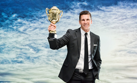 Full length portrait of a young man in a tux holding a golden trophy isolated on white background