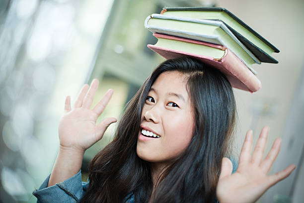 istock Happy Asian girl student balancing stack of books on head. 612511310