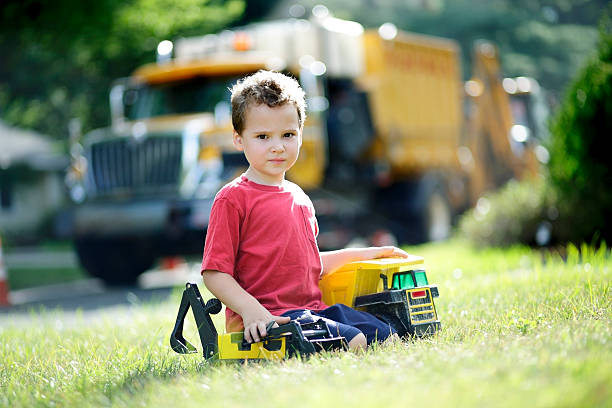 Autistic boy takes a break to interact and make eye contact as he plays with his trucks. Imaginary play is difficult for children like him on the spectrum, but having the real truck on the street in front of his home helped him make a connection.