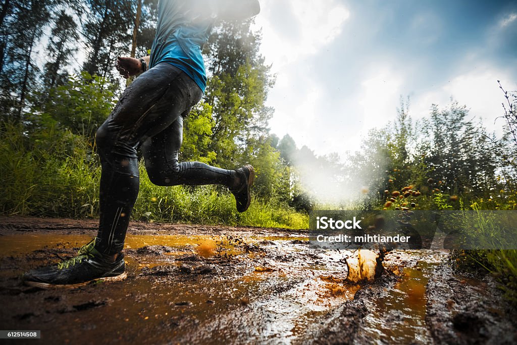 Runner Trial running athlete moving through the dirty puddle in the rural road Mud Stock Photo