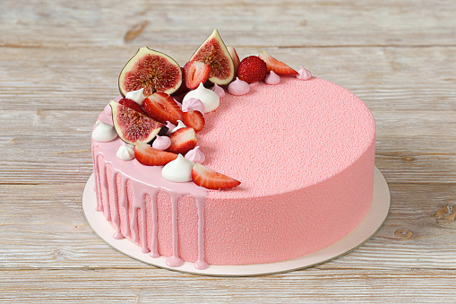 Pink mousse cake covered with pink chocolate velvet and pink mirror glaze, decorated with merinques, strawberry and figs.