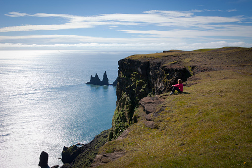 Woman admiring the famous Reynisdrangar rock formations from the cliffs of the mount Reynisfjall, south of Iceland.
