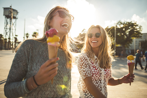 Two women enjoying summer holiday walk and eating an ice cream.