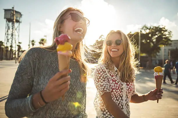 Two women enjoying summer holiday walk and eating an ice cream.