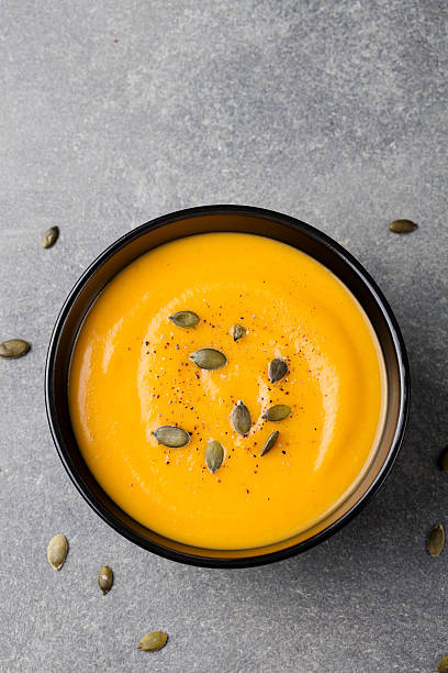 istock Pumpkin cream soup with seeds in a black bowl. 612523322