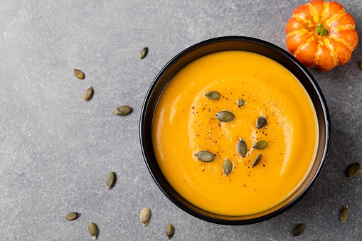 Pumpkin cream soup with seeds in a black bowl.