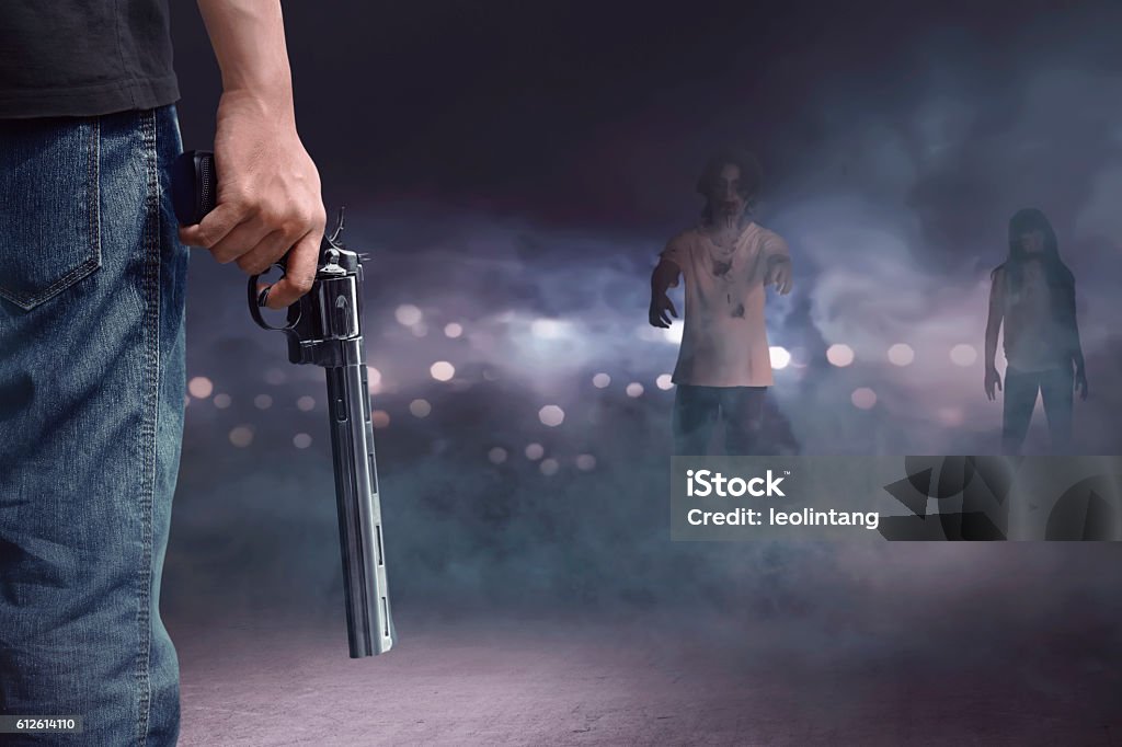 Brave man with jeans pants holding gun looking at zombies Brave man with jeans pants holding gun looking at zombies walking into him Shooting a Weapon Stock Photo