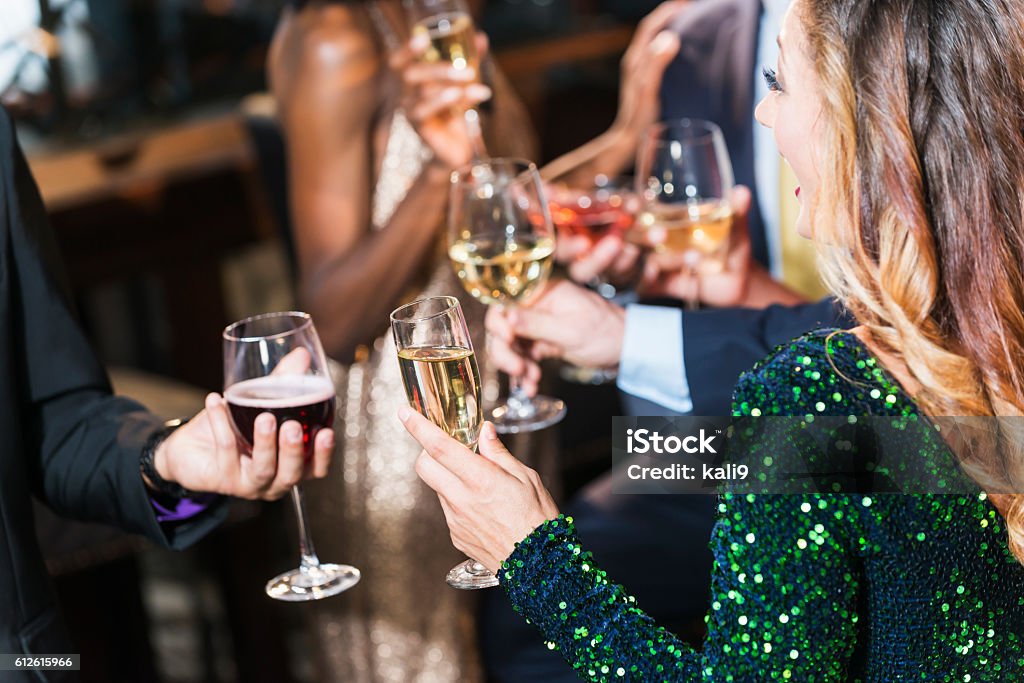 Party scene A multi-ethnic group of young adults drinking together at a bar. The focus is on the woman in the foreground wearing a sequin green dress and holding a champagne flute. Suit Stock Photo