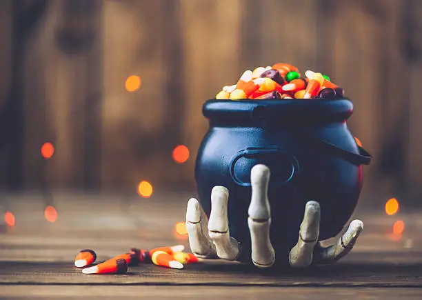 Photo of Halloween still life. Skeletal hand holding cauldron with candy