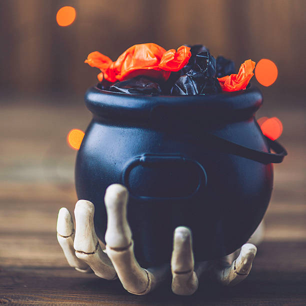 istock Halloween still life. Skeletal hand holding cauldron with candy 612623408