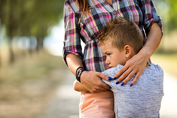 Sad little boy embracing his unrecognizable mother in nature. Worried little boy at the park embracing his unrecognizable mother. worried mom with kids stock pictures, royalty-free photos & images