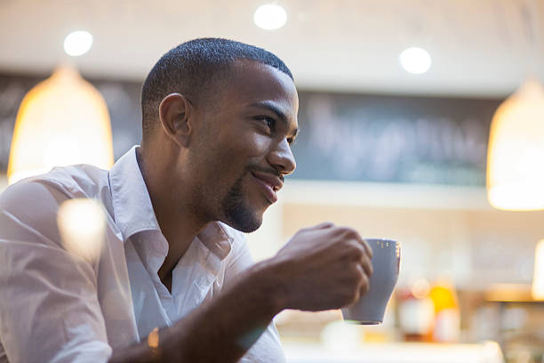 homme afro-américain dégustant une grande tasse de café - homme mug regarder dehors photos et images de collection
