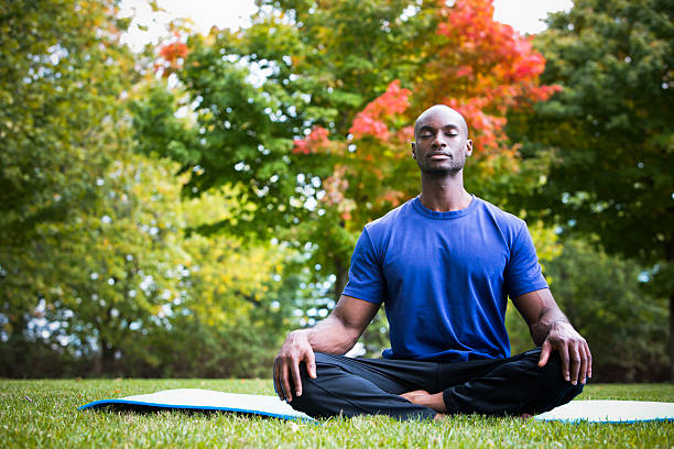 young man exercising yoga young black man wearing athletic wear sitting in the park exercising yoga cross legged stock pictures, royalty-free photos & images