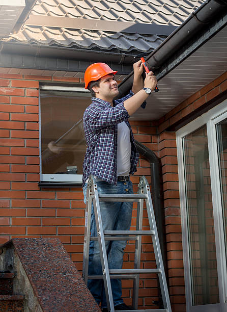 istock Worker standing on step ladder and repairing gutter on house 612653612
