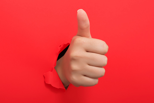 Thumbs up through the paper hole isolated on red background