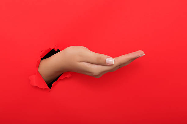 istock Female hand reaching through torn red paper sheet 612656608