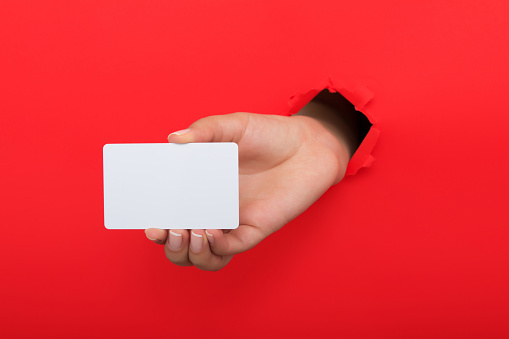 Female hand reaching through torn red paper sheet