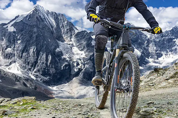 Mountain bike rider with protectors  rides up a single trail in great height. The background shows the "Ortler" mountain massif in the alps.