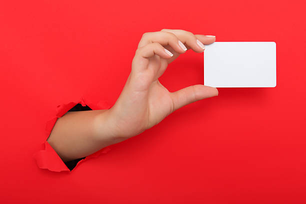 mano femminile che raggiunge attraverso foglio di carta rossa strappato - hole cards foto e immagini stock