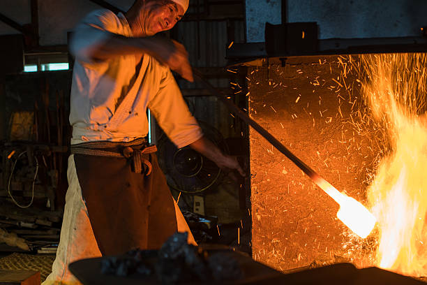 Blacksmith pulls red hot steel from fire to forge sword stock photo