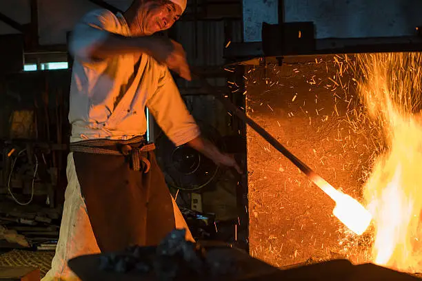 Japanese blacksmith pulls red hot steel from a fire preparing to forge a sword