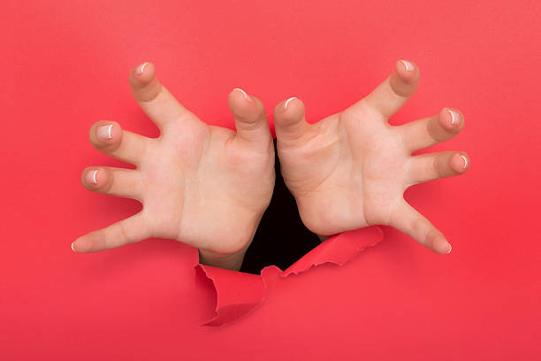 istock Female hand reaching through torn red paper sheet 612716164