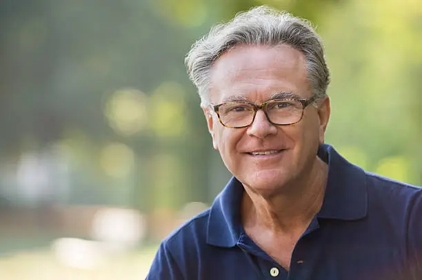 Portrait of senior man smiling and loooking at camera. Face of a happy old man wearing eyeglasses outdoor. Retired man with grey hair relaxing at park during morning.