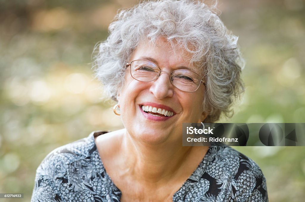 Senior woman laughing Portrait of senior woman smiling and looking at camera. Cheerful mature woman wearing eyeglasses in the park. Happy old woman with grey hair smiling. Carefree and positive retired woman. Senior Women Stock Photo