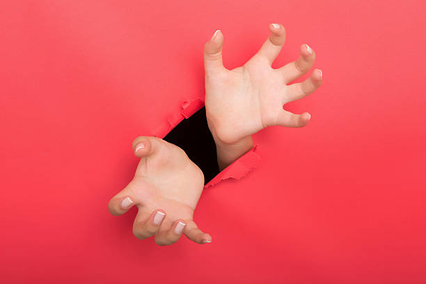 istock Female hand reaching through torn red paper sheet 612717716