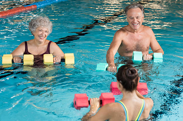 Seniors doing aqua aerobics Senior couple in training session of aqua aerobics using dumbbells in swimming pool. Mature man and old woman practicing aqua fitness together. Healthy and fit senior couple enjoying their retirement in aqua aerobics training. one piece swimsuit photos stock pictures, royalty-free photos & images