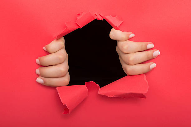 istock Female hand reaching through torn red paper sheet 612719152