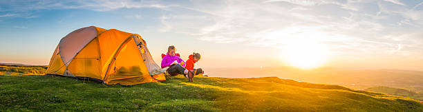 istock Summer sunset camping young hikers beside mountain top tent panorama 612731592