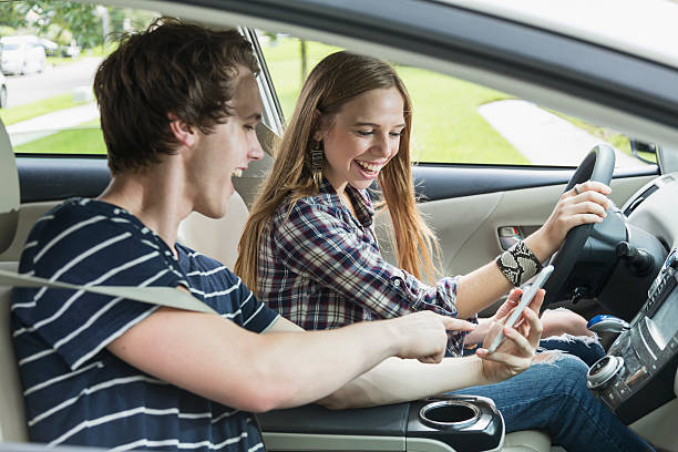 Two teenagers in a car, girl driving Close up of two teenagers in a car. The 17 year old girl in the driver's seat is the focus. The young man in the passenger seat is showing her something on his mobile phone. teenager boy driving stock pictures, royalty-free photos & images