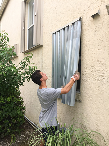 Young man installing hurricane shutters on house window, preparing for hurricane Matthew, Miramar, Florida