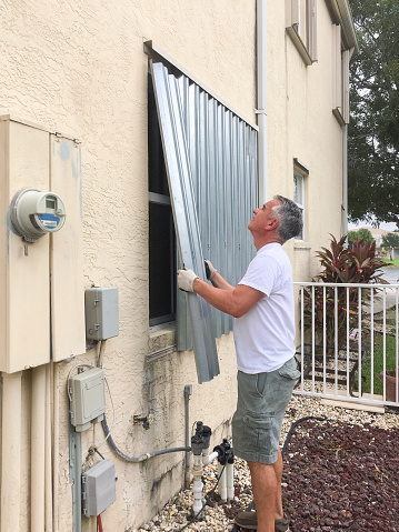 Man installing hurricane metal shutters on house window preparing for hurricane Mathew.