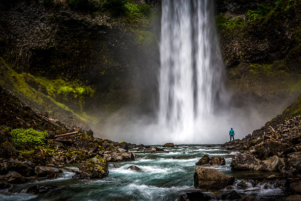uomo in piedi vicino a un'enorme cascata. - waterfall foto e immagini stock