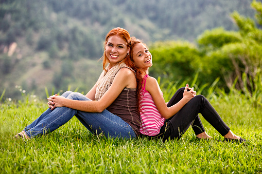 Happy redhead sisters in casual clothing,sitting and having fun outdoors in park. Family and relationships themes.