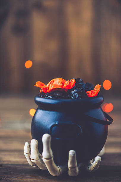 istock Halloween still life. Skeletal hand holding cauldron with candy 612819652