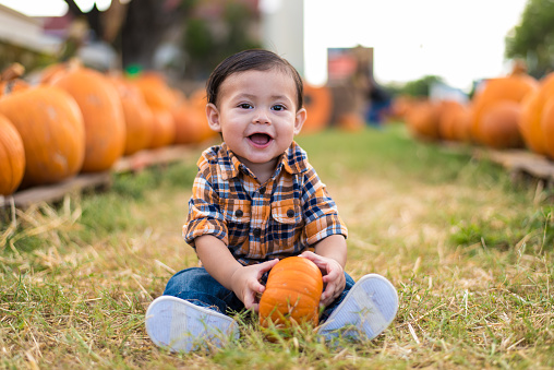 9 month old baby sits at a pumpkin patch at she start of October. 