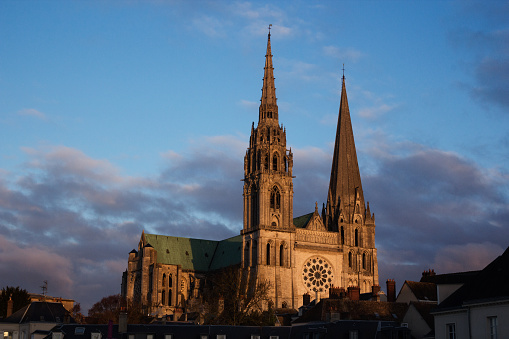 The sun sets on Chartres cathedral, east of Paris, France. The clouds are pink and the light illuminates the main stained glass window of the cathedral. 